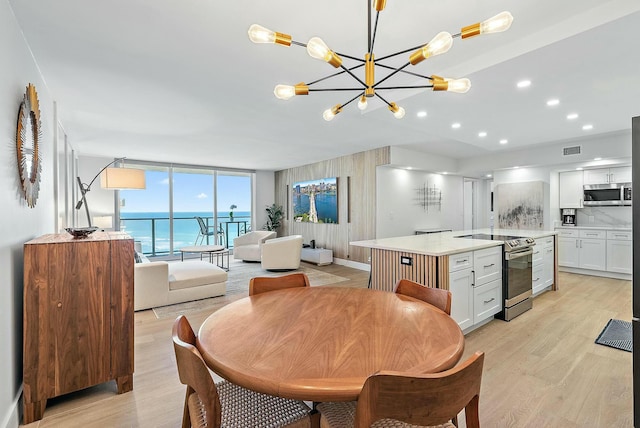 dining room with light hardwood / wood-style floors, a water view, a wall of windows, and a chandelier