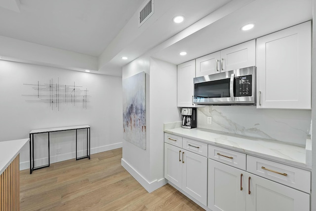 kitchen featuring light stone counters, white cabinetry, backsplash, and light hardwood / wood-style flooring