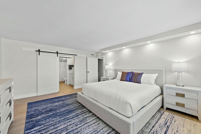 bedroom featuring a barn door, ensuite bathroom, and hardwood / wood-style floors