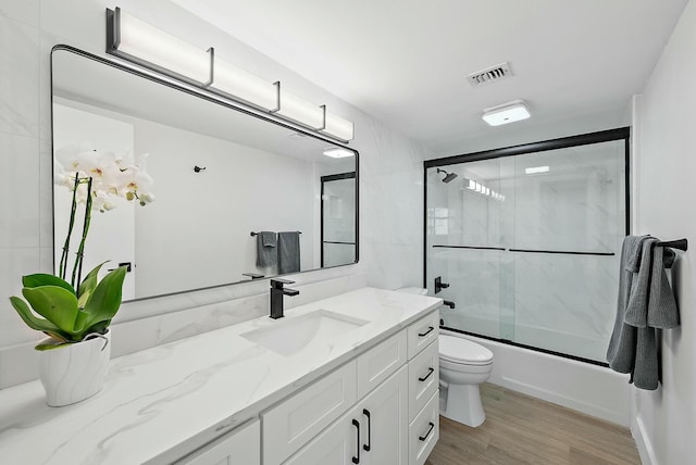 full bathroom featuring toilet, hardwood / wood-style floors, vanity, and combined bath / shower with glass door