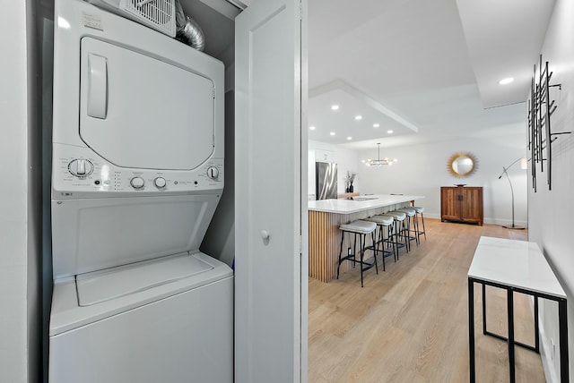 washroom with light wood-type flooring, stacked washing maching and dryer, and an inviting chandelier