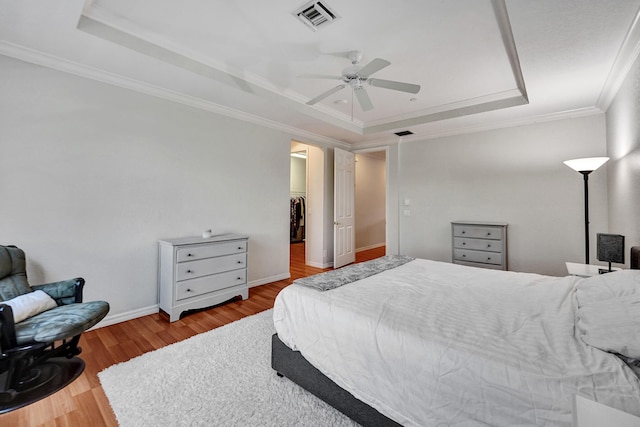 bedroom with ceiling fan, a raised ceiling, a spacious closet, and ornamental molding