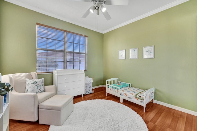 bedroom featuring a crib, hardwood / wood-style flooring, ceiling fan, and crown molding