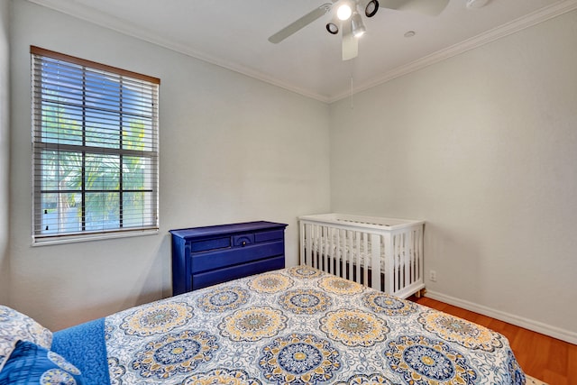 bedroom with ceiling fan, a nursery area, ornamental molding, and hardwood / wood-style flooring