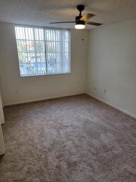 spare room with a textured ceiling, carpet floors, and ceiling fan