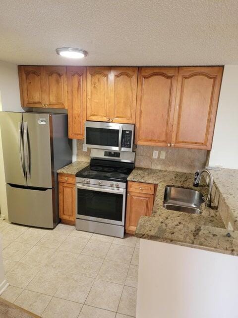 kitchen featuring appliances with stainless steel finishes, a textured ceiling, light stone counters, and sink