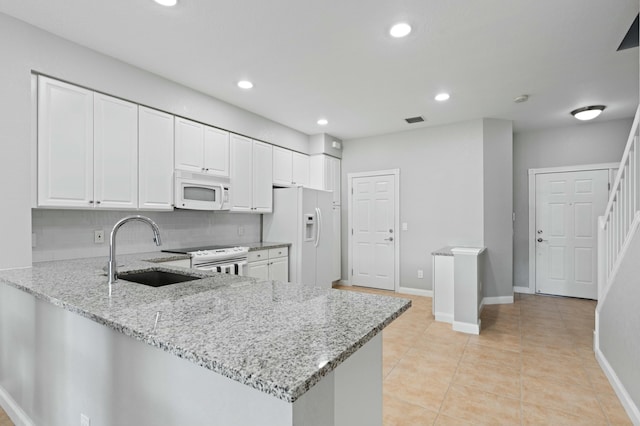 kitchen featuring kitchen peninsula, light stone countertops, white appliances, sink, and white cabinets