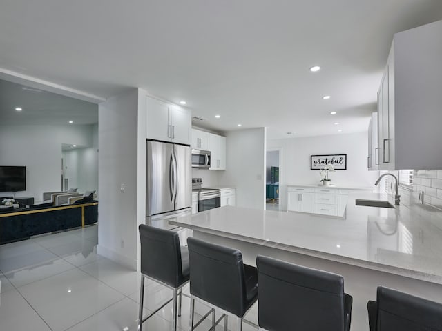 kitchen with a breakfast bar, sink, kitchen peninsula, appliances with stainless steel finishes, and white cabinetry