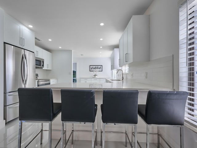 kitchen with white cabinetry, sink, stainless steel appliances, kitchen peninsula, and a kitchen bar