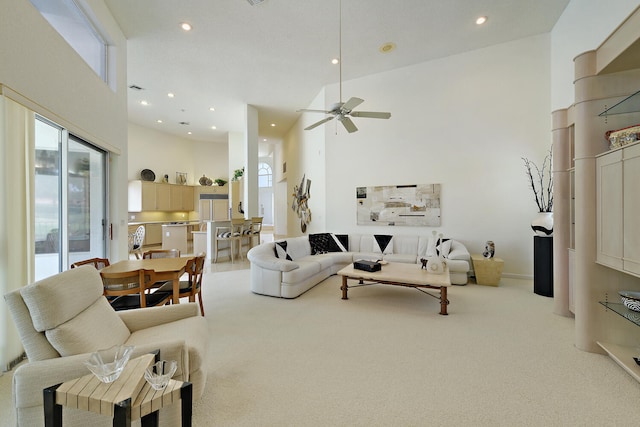 living room with ceiling fan, light colored carpet, and a towering ceiling