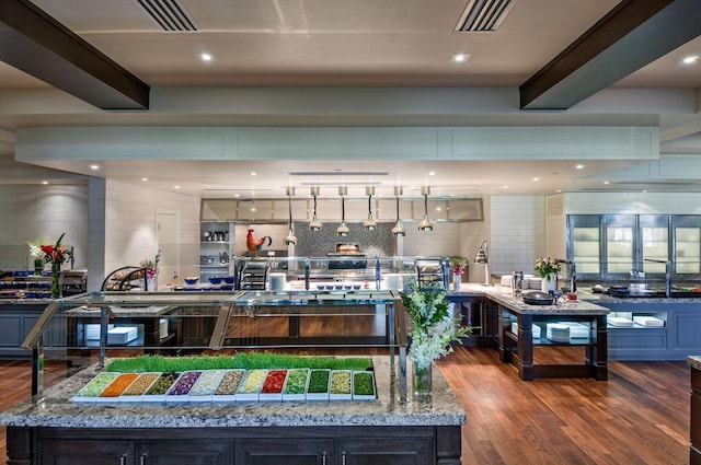 kitchen featuring light stone countertops, decorative backsplash, a spacious island, wood-type flooring, and beamed ceiling