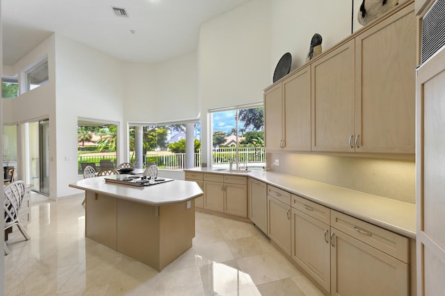 kitchen with a towering ceiling, light brown cabinetry, a center island, and sink