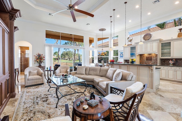 living room featuring a towering ceiling, ornamental molding, ceiling fan, and a tray ceiling