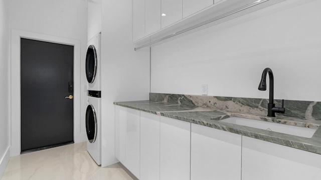 clothes washing area with cabinets, stacked washer and dryer, and sink