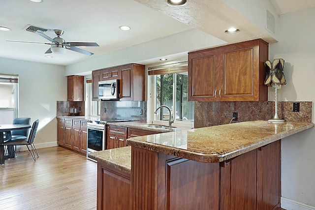 kitchen featuring decorative backsplash, a peninsula, stainless steel appliances, light wood-type flooring, and a sink