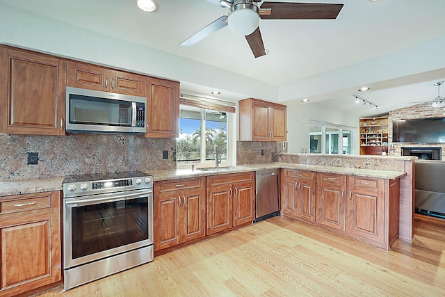 kitchen with stainless steel appliances, light wood-style flooring, open floor plan, a sink, and a peninsula