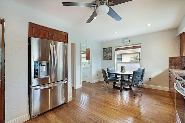 kitchen featuring appliances with stainless steel finishes, washing machine and clothes dryer, light wood-style flooring, and baseboards