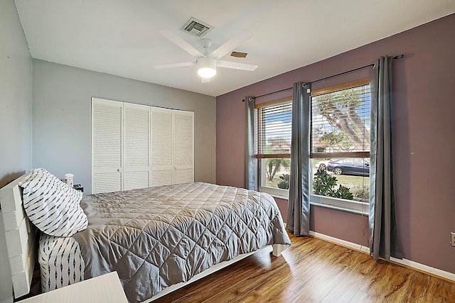 bedroom with a closet, visible vents, baseboards, and wood finished floors