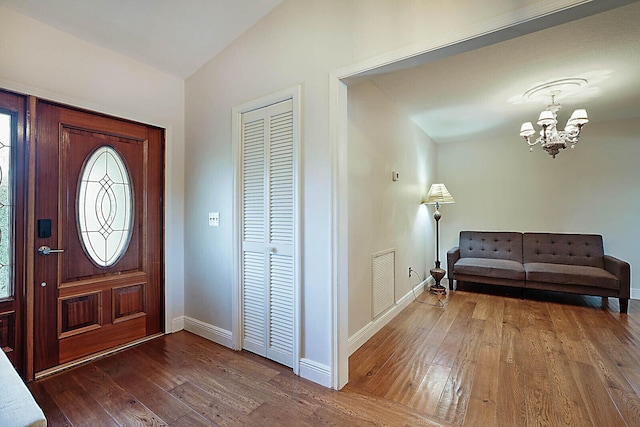 foyer entrance with baseboards, visible vents, wood-type flooring, vaulted ceiling, and a notable chandelier