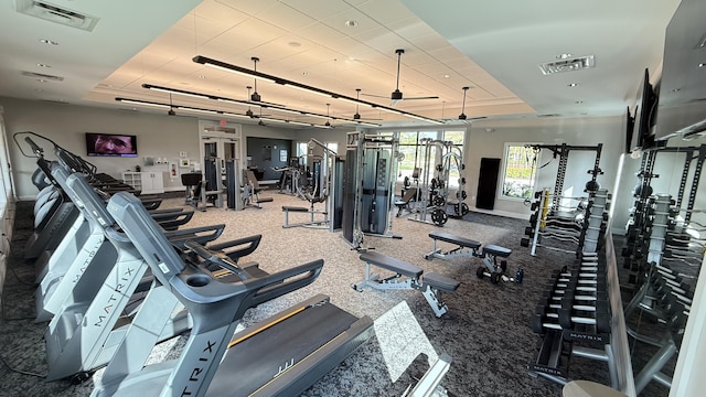 exercise room with ceiling fan and a tray ceiling