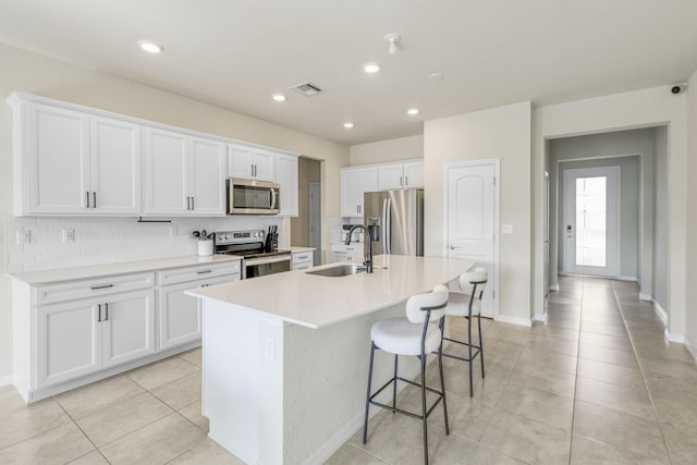 kitchen with a kitchen island with sink, sink, appliances with stainless steel finishes, tasteful backsplash, and white cabinetry