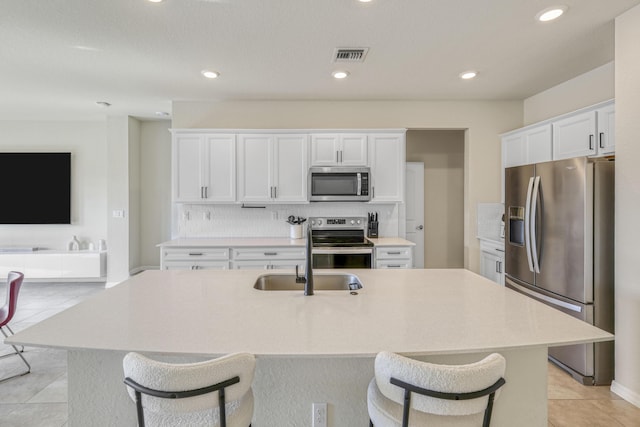 kitchen with white cabinetry, tasteful backsplash, a kitchen island with sink, light tile patterned floors, and appliances with stainless steel finishes