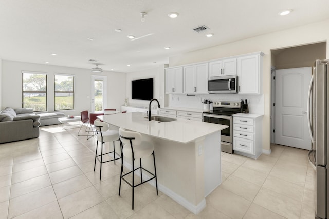 kitchen featuring white cabinetry, sink, backsplash, a kitchen island with sink, and appliances with stainless steel finishes