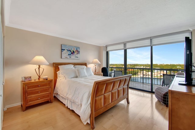 bedroom with access to exterior, a textured ceiling, light wood-type flooring, and floor to ceiling windows