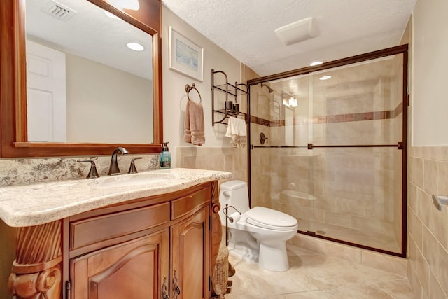 bathroom with a textured ceiling, vanity, an enclosed shower, and tile walls