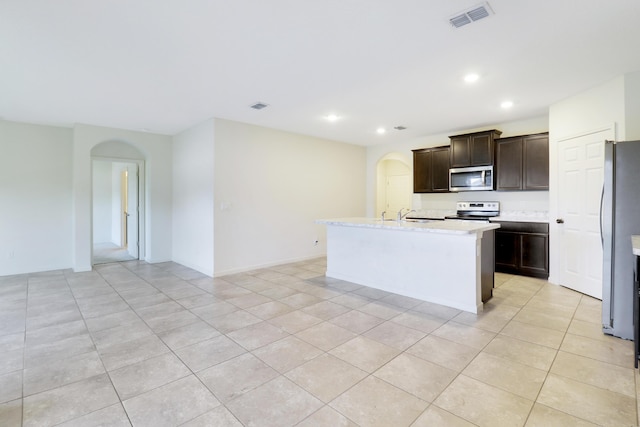 kitchen featuring sink, dark brown cabinets, light tile patterned floors, appliances with stainless steel finishes, and a kitchen island with sink