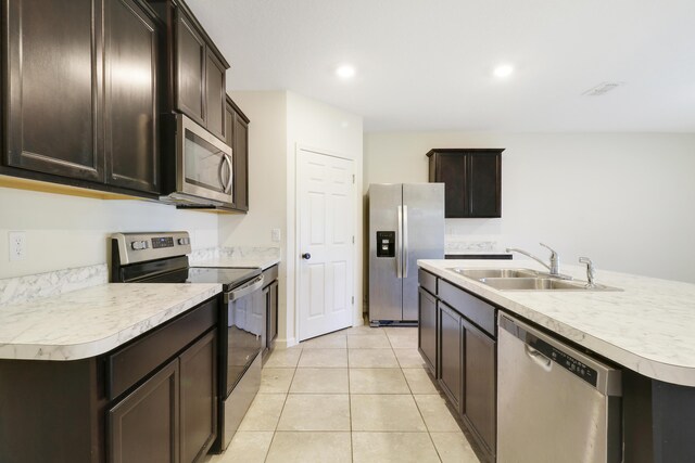 kitchen with light tile patterned flooring, sink, dark brown cabinets, a center island with sink, and appliances with stainless steel finishes