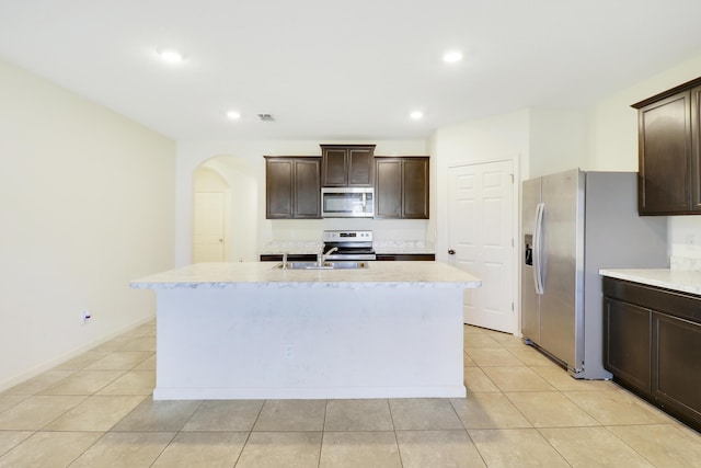 kitchen with appliances with stainless steel finishes, sink, a center island with sink, and dark brown cabinetry