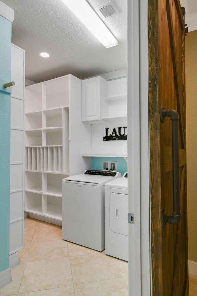 washroom with cabinets, a textured ceiling, washer and clothes dryer, a barn door, and light tile patterned flooring