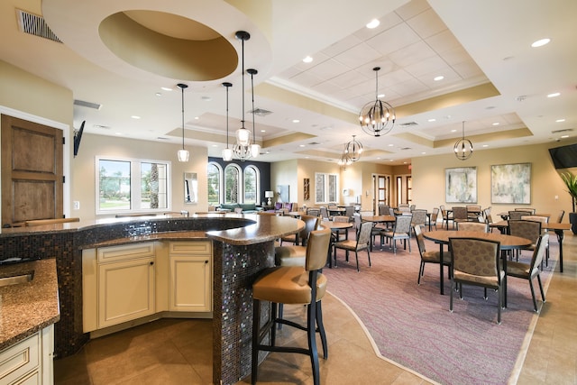 kitchen featuring pendant lighting, an inviting chandelier, a raised ceiling, dark stone countertops, and cream cabinetry