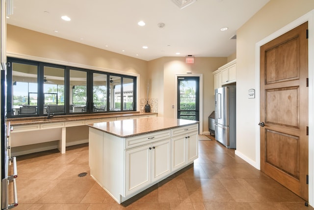 kitchen featuring white cabinetry, a center island, light stone countertops, high end refrigerator, and decorative backsplash