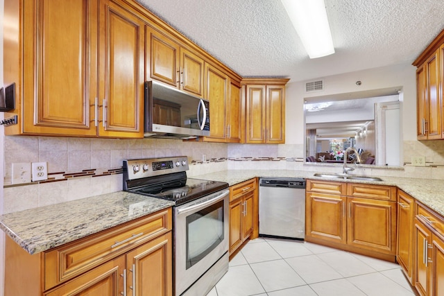 kitchen with light stone countertops, sink, stainless steel appliances, a textured ceiling, and light tile patterned floors