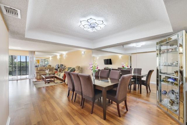 dining space with hardwood / wood-style floors, a textured ceiling, and a tray ceiling