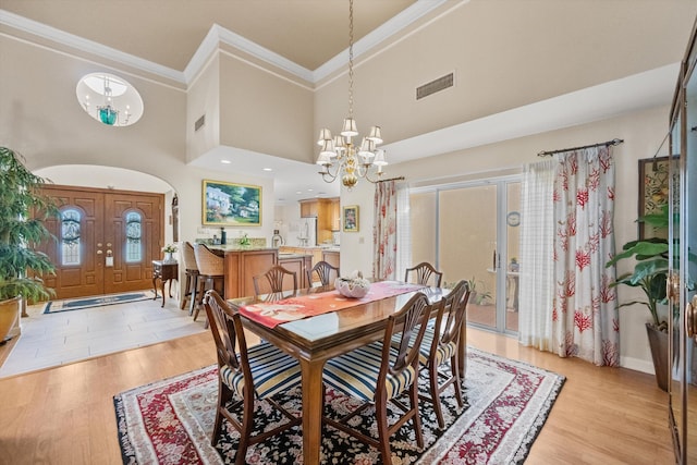 dining area with light hardwood / wood-style floors, an inviting chandelier, a towering ceiling, and crown molding