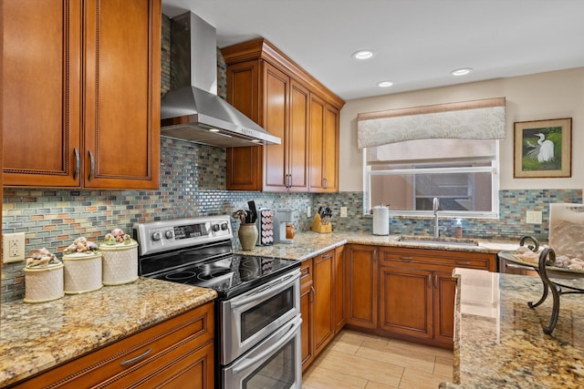 kitchen with sink, decorative backsplash, range with two ovens, light stone countertops, and wall chimney range hood