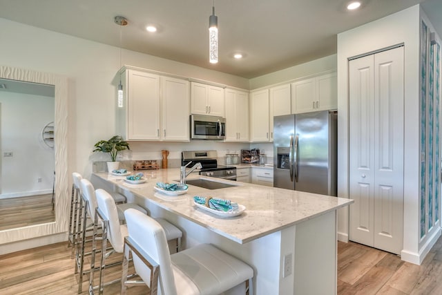 kitchen featuring a breakfast bar, sink, appliances with stainless steel finishes, decorative light fixtures, and white cabinetry