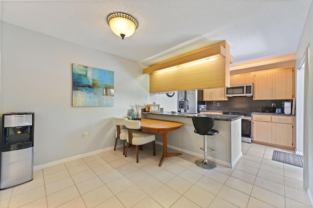 kitchen with kitchen peninsula, a kitchen bar, decorative backsplash, light brown cabinetry, and range