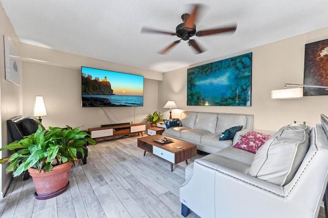 living room featuring ceiling fan, a textured ceiling, and light wood-type flooring