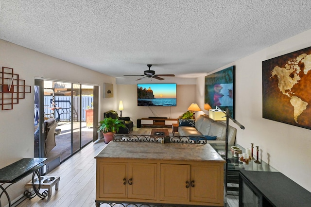 living room featuring ceiling fan, light hardwood / wood-style floors, and a textured ceiling