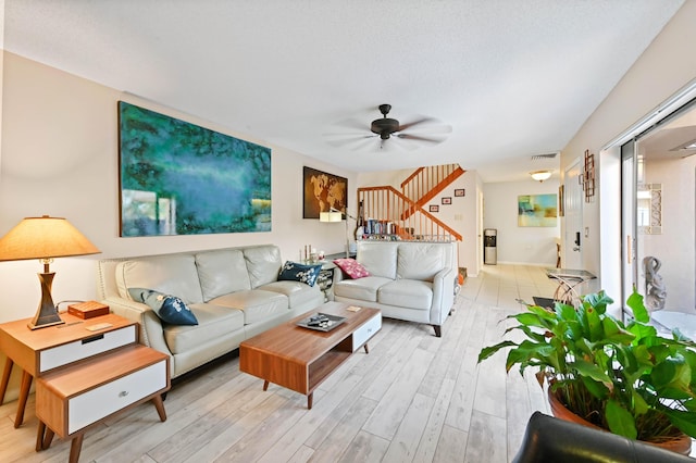 living room featuring ceiling fan, light wood-type flooring, and a textured ceiling