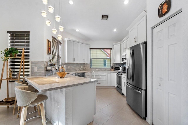 kitchen featuring stainless steel appliances, a kitchen breakfast bar, decorative backsplash, white cabinets, and decorative light fixtures