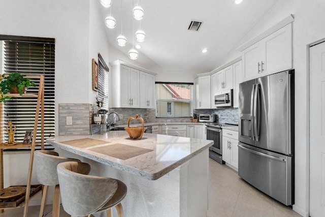 kitchen with white cabinetry, vaulted ceiling, a kitchen breakfast bar, kitchen peninsula, and stainless steel appliances