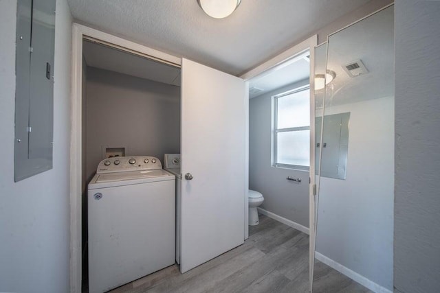 washroom with washer / clothes dryer, electric panel, a textured ceiling, and light wood-type flooring