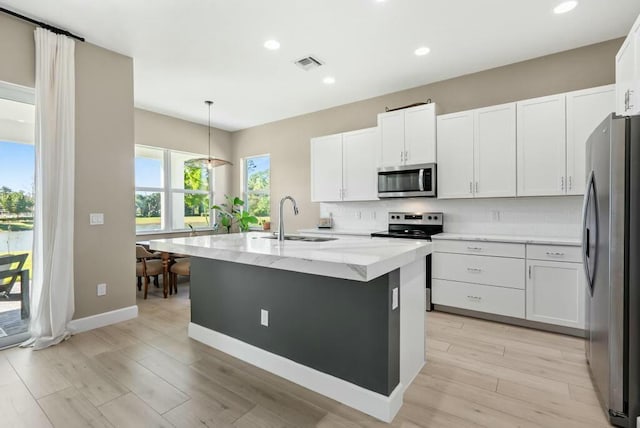 kitchen with stainless steel appliances, sink, pendant lighting, a center island with sink, and white cabinetry