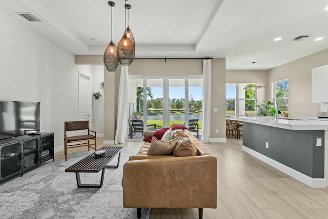 living room with a raised ceiling, sink, and light wood-type flooring