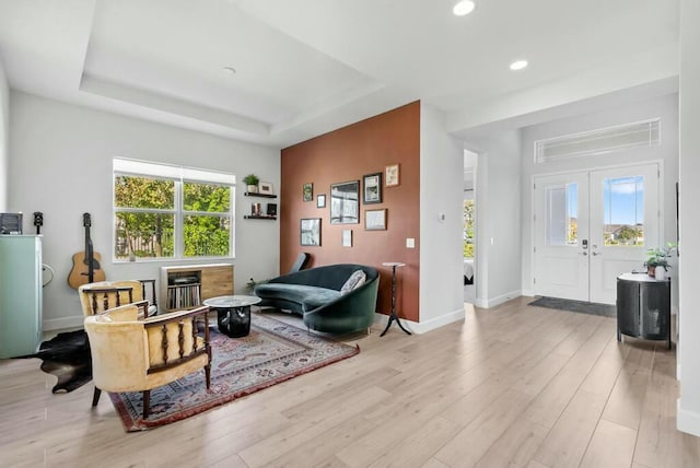 living room featuring light wood-type flooring, a tray ceiling, and french doors